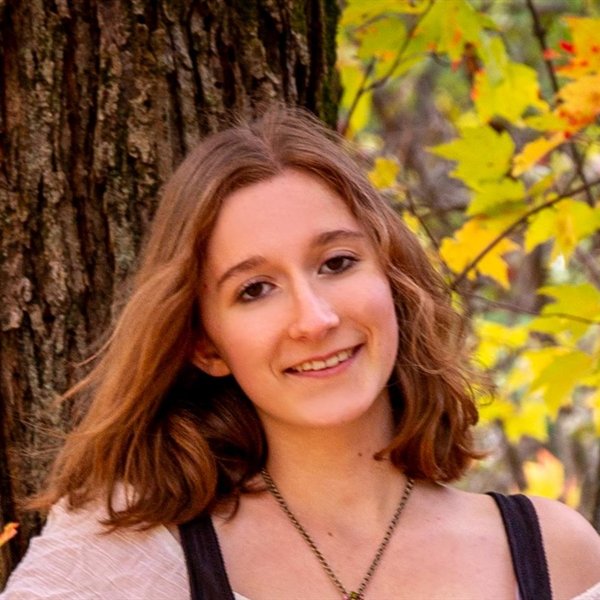 Claire Metcalfe in front of a tree trunk and fall maple leaves